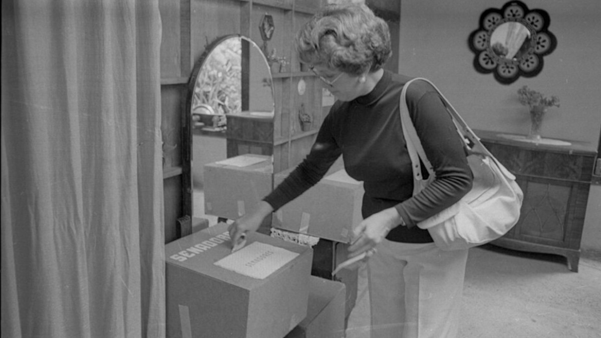 Frau steckt Wahlkärtchen in Wahlurne